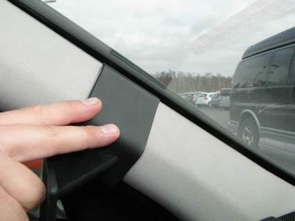 En hand som håller i en svart detaljerad del vid vindrutan på en bil.