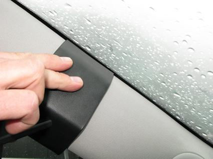 En hand trycker på en svart plastdetalj vid bilfönstret. Regn vatten på glaset.