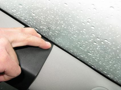 En hand trycker på ett material vid en bilruta med regndroppar.