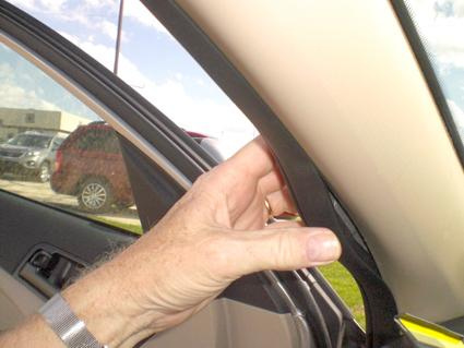 En hand håller i en del av bilens inredning vid dörren.