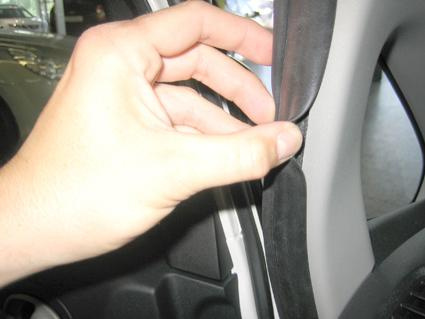 En hand håller i en gummitätning på en bils dörr.