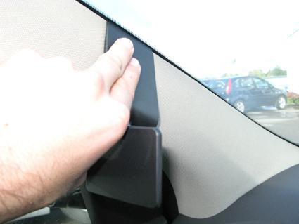 En hand trycker mot en plastdetalj i bilens inredning, nära vindrutan.