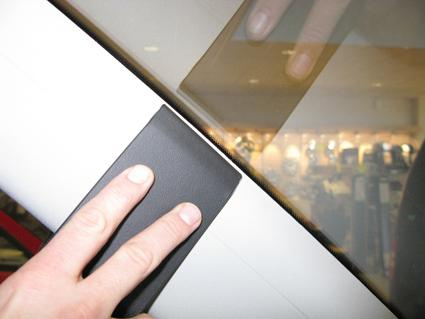 Svart detalj på bilens fönsterkarm med en hand som visar placering.