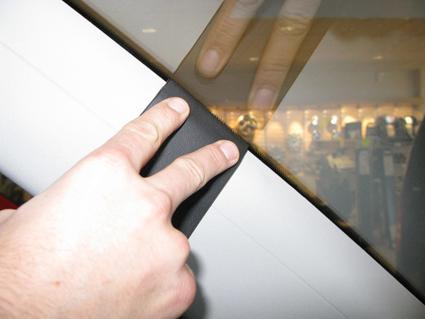 En hand trycker mot en svart gummitätning på en bilfönsterkant.