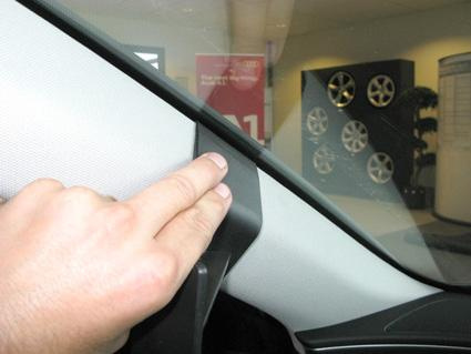 En hand pekar på en del av bilens interiör, nära vindrutan.