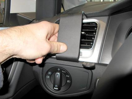 En hand håller i en del av en bilkonsol för Volkswagen Golf VII.