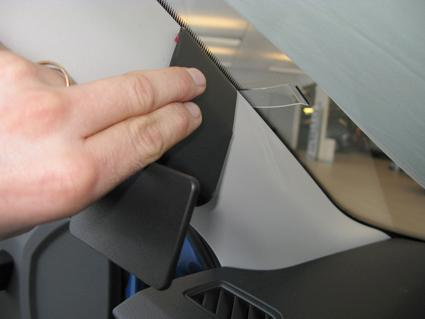 En hand håller i en svart plastdel nära fönsterrutan i en bil.