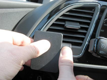 En hand håller en svart del mot luftutblåset i en bil.