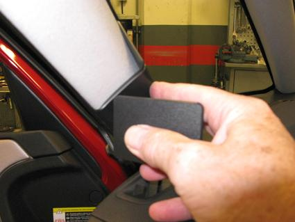 En hand håller en svart bricka nära en bils inre spegel.