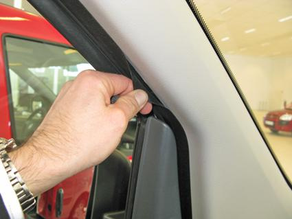 Hand som justerar en tätning eller panel nära fönsterramen i en bil.