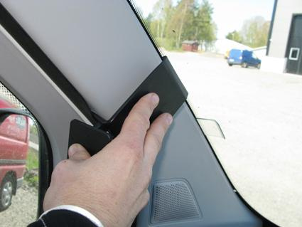 En hand håller i en svart infästning vid bilens A-stolpe.