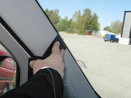 En hand som pekar mot en del av en bilinteriör, nära vindrutan.