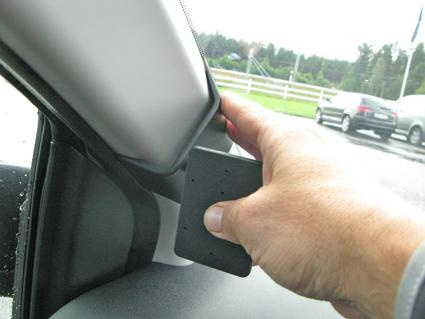 Hand som håller en svart del mot bilens inre hörn vid fönstret.