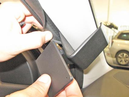 En hand håller en svart komponent vid bilens fönsterkant.