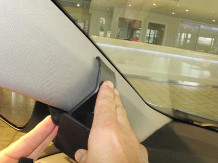 En hand håller i en svart detalj som monteras vid vindrutan.