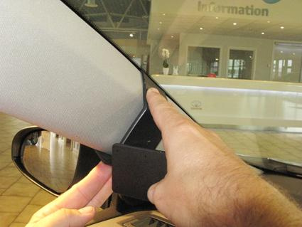 Hand som håller i en del av en bilinteriör, troligen vid backspegelsfästet.