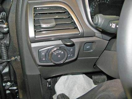 En kontrollpanel med olika knappar och en ratt, troligen för inställningar i en bil.