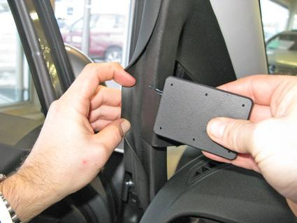 En hand som håller en svart del nära bilens interiör.