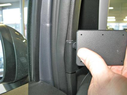 En hand håller en svart komponent nära bilens dörrstolpe.