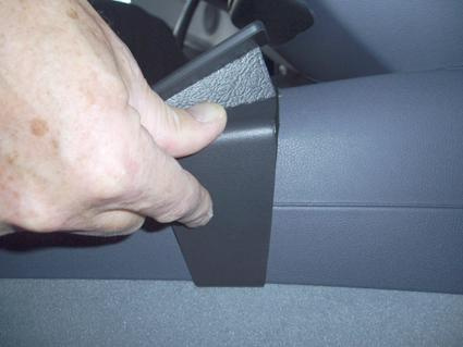 En hand håller i en svart konsolbit för BMW 1 E81/E82/E87/E88.