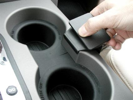 En hand som lyfter en del av en armstödkonsol med två kopp-hållare.