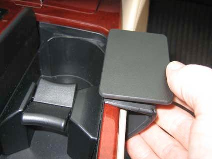 En hand håller ett avtagbart lock över en förvaringsplats i en bilkonsol.