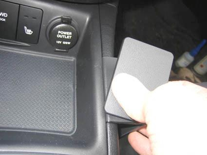 En hand som lyfter en panel i en bilkonsol med knappar och uttag.