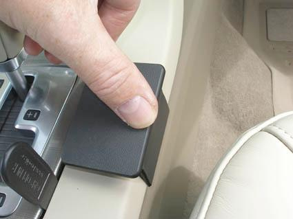 En hand trycker på en svart konsoldel i en bil.