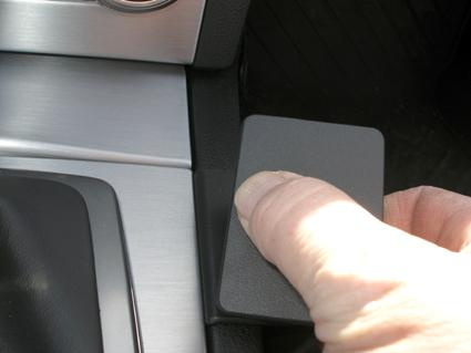 En hand som trycker på en svart knapp i en bilkonsol.