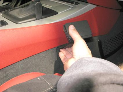 En hand sträcker sig efter en svart konsol i en bilinteriör.
