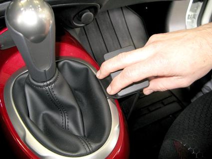 Manuell växelspak med läderklädsel och en hand som trycker på en knapp.