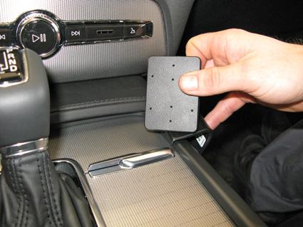 En hand håller en fyrkantig enhet över en konsol i en Volvo XC90.