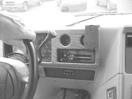 En hand som håller i ratten, del av en bilinteriör med instrumentpanel.