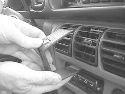 En hand håller en del av en bils instrumentpanel, nära luftventiler.