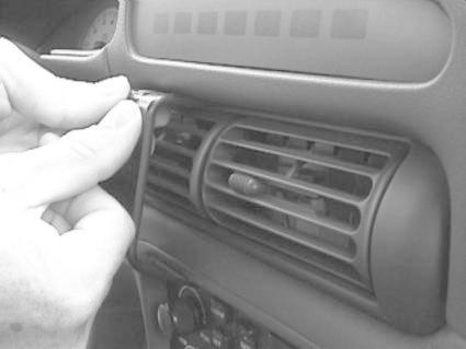 En hand fäster en monteringsbygel vid luftventilen i en bil.