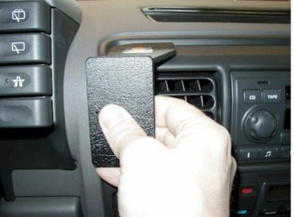 En hand håller en monteringsbygel på bilens instrumentbräda.