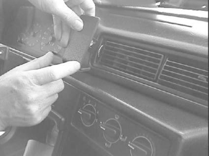 En hand håller i en svart enhet nära bilens klimatkontroll och luftutlopp.