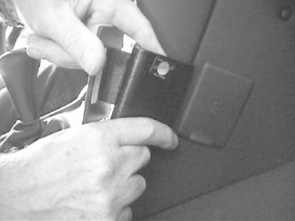 Ett par händer installerar eller justerar en säkerhetsbältesdel i en BMW Z3.