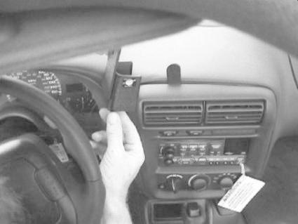 En hand håller en monteringsbygel inuti en bil, fokus på instrumentpanelen.