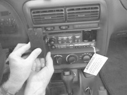 En hand håller en monteringsbygel vid bilens ljudsystem.