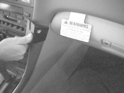 En hand håller en vinklad del vid bilens invändiga hörn med en varningsskylt.