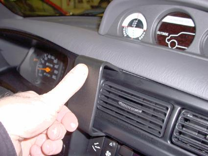 En hand pekar på en plastdetalj på bilens instrumentpanel.