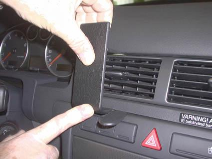 En hand håller en svart plastdel som ska monteras i Audi A6:s mittkonsol.