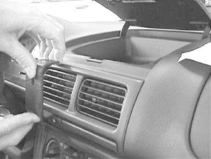 En hand installerar en detalj i bilens inredning nära luftventilerna.