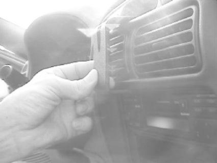 En hand håller en monteringsbygel vid en bils luftventil.