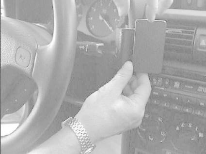 En hand håller en svart enhet vid bilens mittkonsol.