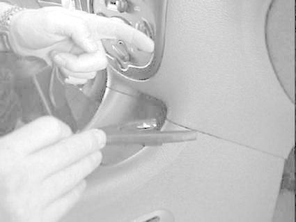 En hand som pekar och håller ett verktyg nära en bilkomponent.