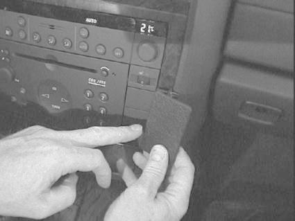 Bild av en hand som pekar på bilradio i en Opel Omega, med en liten enhet i andra handen.