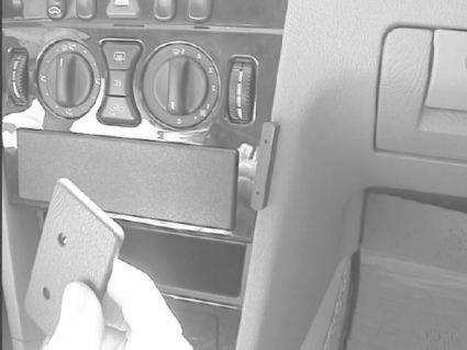 En hand som håller en fyrkantig del inuti bilen, nära kontroller och förvaringsutrymme.