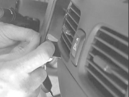 En hand justerar en knapp nära luftventiler i en bilinteriör.
